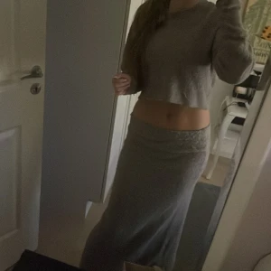 Grå/lila  långkjol och topp i stickat material - Säljer en mjuk och mysig grå/lila långkjol med en matchande tröja i stickat material. Kjolen har en rak och slim passform som sitter snyggt över höften och faller rakt ner mot anklarna. Perfekt att matcha med den croppade stickade tröjan för en chill och stilren look.