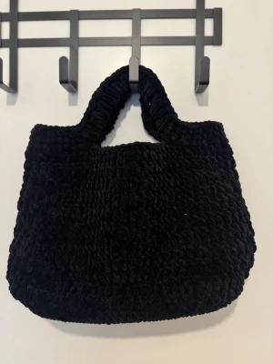 Svart fluffig handväska i sammet - Säljer en svart handväska med mjuk och fluffig känsla i sammet. Väskan har rundad form, breda handtag och en stadig botten. Perfekt storlek för att få plats med allt du behöver så som en 15 tums laptop och ger en cool vibe till din outfit.