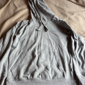 Grå hoodie från Pepe Jeans - Säljer en stilren grå hoodie från Pepe Jeans med klassisk känguruficka och dragsko i huvan. Tröjan är i mjuk bomull och har diskret logga på bröstet. Perfekt för chill dagar eller när du vill ha en enkel och snygg look.