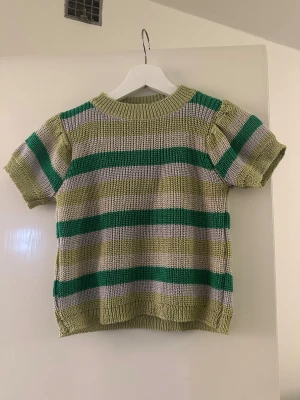 Randig stickad T-shirt från RUDE - Säljer en stickad T-shirt från RUDE med breda gröna, gråa och ljusgröna ränder. Tröjan har korta ärmar och rund hals. Perfekt för dig som gillar retrovibbar och vill sticka ut med färg. Det står ingen storlek i tröjan men skulle säga XXS/XS!