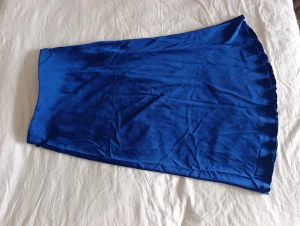Blå långkjol i satin från Lindex - Snygg blå långkjol från Lindex i glansigt satinliknande material. Kjolen har en lätt utsvängd form och vågig kant nertill som ger en flowing och lätt look.