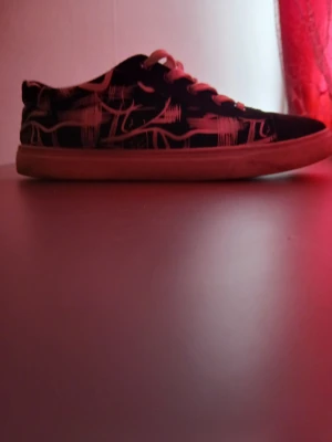 Svarta sneakers med vit grafisk print - Säljer ett par svarta sneakers med vit grafisk print och vita snören. Skorna har rund tå, platt sula och coolt mönster som sticker ut. Perfekt för dig som gillar streetstyle och vill ha något unikt på fötterna.
