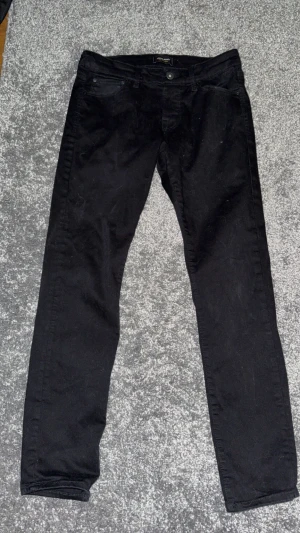 Svarta jeans från Jack & Jones - Svarta jeans från Jack & Jones i klassisk femficksmodell. Byxorna har en smal passform och raka ben, tillverkade i mjuk bomullsblandning med lite stretch för extra komfort. Perfekta för dig som gillar en stilren och enkel look.