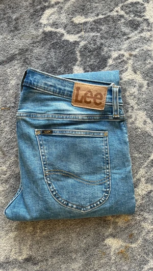 Blå Lee jeans Luke - Snygga blå jeans från Lee med klassisk femficksdesign och brunt Lee-märke bak i midjan. Jeansen har rak passform och är tillverkade i slitstarkt denimtyg med ljus tvätt. Midja: 42cm Längd: 97cm Bredd vid benöppning: 16cm