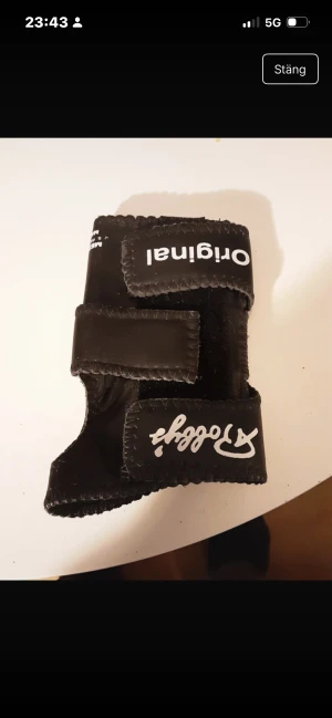 Svart träningshandske Stobby Original - Svart träningshandske från Stobby Original med vit logga och text. Handsken har en robust design med breda kardborreband för extra stöd runt handleden. Perfekt för gym eller styrketräning där grepp och skydd behövs.