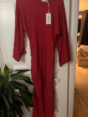 Röd strukturerad maxiklänning NA-KD - Maxiklänning från NA-KD i storlek 38. Klänningen har lång ärm, strukturerat tyg och en dragskoslits längst ner. Perfekt till julens alla firanden! 🎅🎄