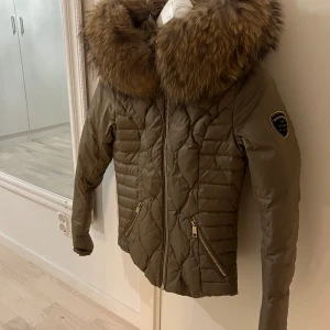 Dunjacka med pälskrage från RockandBlue - Säljer en snygg beige dunjacka från Rockandblue med en stor, fluffig och äkta pälskrage. Storlek 32 men skulle säga att den passar som en 34. Jackan har en quiltad design och dragkedjor på fickorna. Perfekt för kalla vinterdagar! 🧥❄️