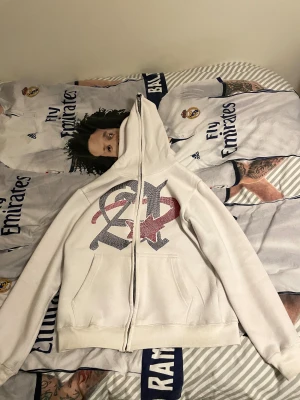 Vit hoodie Aim For The Moon M - Säljer en vit hoodie från Aim For The Moon i storlek M. Tröjan har dragkedja hela vägen, huva och två fickor framtill. På bröstet finns ett stort tryck i svart och rött. Mjuk insida i fleece och klassisk passform.