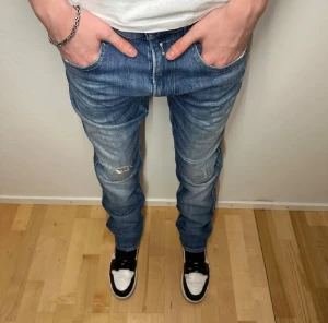 Blå replay ambass med slitningar - Säljer ett par blå replay ambass jeans med snygga slitningar och en liten reva på vänster knä. Jeansen har normal passform, klassisk femficksdesign och är tillverkade i mjukt denimtyg. Perfekta för dig som gillar en avslappnad men ändå stilren look.