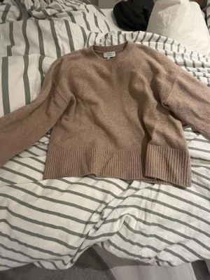 Beige stickad tröja från & Other Stories - Mysig beige stickad tröja från & Other Stories med breda ribbade muddar vid ärmslut och nederkant. Tröjan har en avslappnad passform och rund halsringning, perfekt för lager på lager under kyliga dagar.