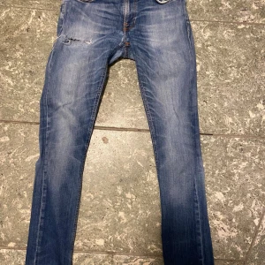 Nudie jeans - Säljer ett par blå nudie jeans för endast 350 kr. Jeansen har en slitning på framsidan. Jeansen är i storlek 30-34. Dessa jeans passar perfekt nu till hösten med sin vintage look.
