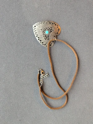 Halsband med hjärtdetalj - Halsband med en stor hjärtformad metallplatta framtill, dekorerad med ett turkost stencenter och utskurna mönster. 