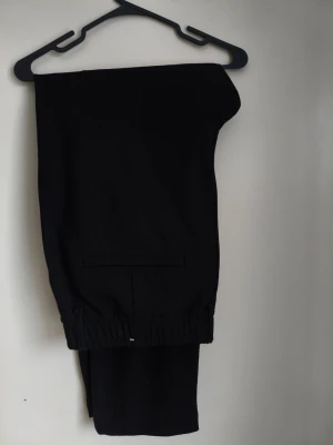 Svarta dressade byxor från Zara - Svarta dressade byxor från Zara i storlek XL med elastisk midja och knäppning fram. Byxorna har en rak passform, sidfickor och är tillverkade i ett mjukt material som ger en clean och stilren look. Perfekta för dig som gillar enkel och snygg stil. Eleganta men väldigt bekväma.