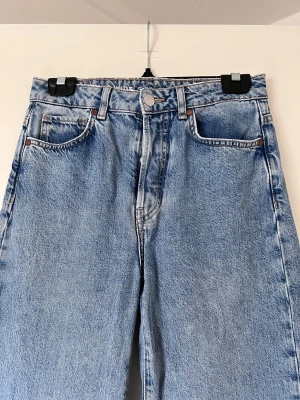 Blå jeans från Bikbok, storlek W28 L32 - Snygga blå jeans med hög midja och rak passform. Klassisk femficksdesign med knapp och dragkedja framtill. Perfekta för en avslappnad stil. Använda 1 gång! Önskar du veta exakta mått? Tveka inte att höra av dig!