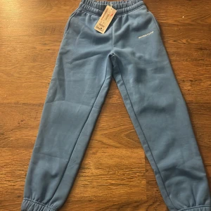 Blå mjukisbyxor från fb sisters - Snygga mjukisbyxor i ljusblå färg från fb sisters. Byxorna har elastisk midja och muddar vid bensluten för en skön och avslappnad passform. Perfekta för chill dagar och har en enkel design med diskret logga på höften. Passar upp till storlek s. Köpt för 150 på rea