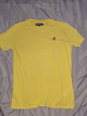 T-shirt från Lyle & Scott - Gul t-shirt från Lyle & Scott junior med logga broderad på bröstet och har en clean, enkel look som funkar till jeans eller shorts.