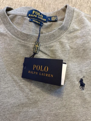 Grå sweatshirt från Polo Ralph Lauren - Snygg grå sweatshirt från Polo Ralph Lauren med klassisk rund hals och långärmad passform. Står L men är  Liten i storlek 