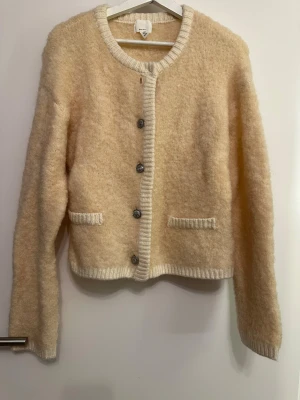 Beige ullkofta från H&M med knappar i stl s  - Mysig beige kofta i stl s från H&M i ullblandning med ribbade detaljer vid krage, knappslå och fickor. Koftan är helt ny aldrig använd. 