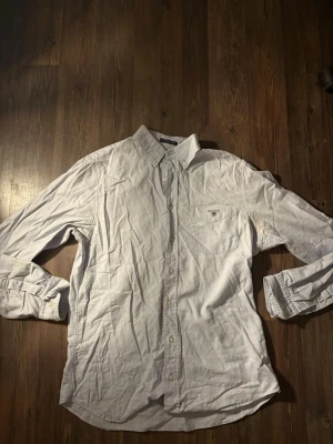 Ljusblå oxfordskjorta från Gant - Klassisk Ljusblå oxfordskjorta från Gant med button down-krage och bröstficka med broderad logga. Skjortan har långa ärmar och stängs med pärlemorskimrande knappar. Perfekt för en clean och stilren look.