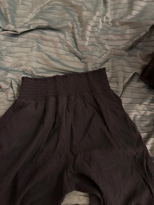 Svarta vida linnebyxor med resårmidja - Säljer ett par svarta linnebyxor med bred resår i midjan och vid benslut. Byxorna har en skön, luftig passform och är tillverkade i ett krinklat linnematerial som ger en cool textur. Perfekta för dig som gillar avslappnad och trendig stil.