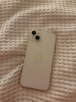 iPhone 14 Plus - Snygg vit iPhone 14 Plus i mycket fint skick. Telefonen har dubbla kameror, fräsch baksida och rena kanter utan synliga repor eller bucklor. Skärmen fungerar och visar Apple-loggan vid uppstart. Perfekt för dig som vill ha en modern och pålitlig smartphone.