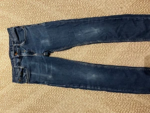 Blå skinny jeans från Marc O'Polo - Snygga blå jeans från Marc O'Polo i storlek 152. Modellen är skinny med klassisk femficksdesign och coola slitningar framtill. Jeansen har normal passform och är tillverkade i mjukt denimtyg med detaljerade sömmar och läderpatch bak i midjan.