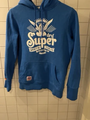 Superdry Hoodie  - En skitfet Superdry Hoodie i storlek M med slim fit passform och ett snyggt tryck på bröstet! Hör av dig vid fler frågor eller bilder😃
