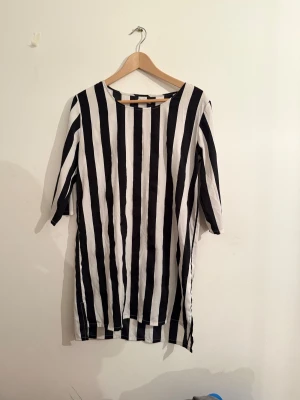 Svartvit randig klänning från Cubus  - Svartvit klänning med breda vertikala ränder från Cubus . Modellen är rak med rund halsringning och har halvlånga ärmar. Klänningen är i kort längd och har en stilren, grafisk look som sticker ut. Perfekt för dig som gillar att synas och vill ha något unikt.