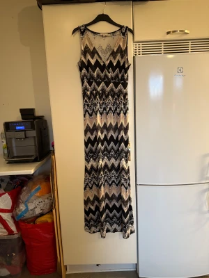 Lång mönstrad klänning från Cream - Snygg långklänning från Cream i svart, beige och grått med coolt zigzag-mönster. Ärmlös modell med v-ringning och mjukt, stretchigt material som sitter skönt. Perfekt för dig som gillar unika mönster och vill sticka ut. Storlek M. Mycket fint skick, jag hittar inga synliga anmärkningar eller defekter. 
