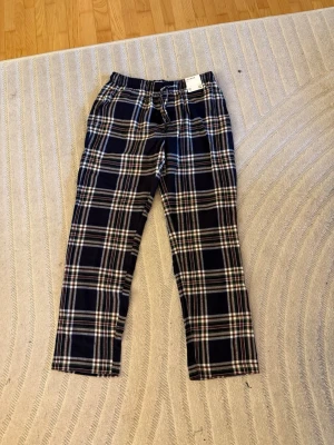 Rutig loungebyxa i bomull, storlek L - Mysiga rutiga loungebyxor i mörkblått, grönt, vitt och rött. Byxorna har dragsko i midjan och är tillverkade i mjuk bomull. Perfekta för chill dagar hemma eller som pyjamasbyxa.