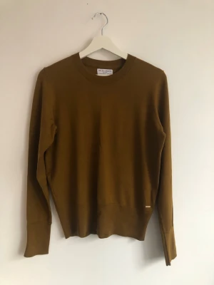Guldbrun/senapsbrun tröja - Helt ny tröja från Holly & Whyte. Stl M. Inga anmärkningar, jättefin.   77% tencel lyocell  23% polyester  Övervidd: 50 cm Längd: 60 cm
