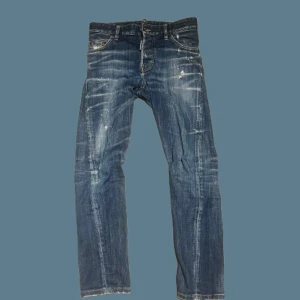 Blå Dsquared2 jeans med slitningar - Snygga blå jeans från Dsquared2 med coola slitningar och ljusa tvättade detaljer. Klassisk femficksmodell med raka ben och läderpatch bak i midjan. Jeansen har en trendig, lite sliten look och är tillverkade i bomullsdenim. Orginalpris från 4400 sek.Midjemått 76 cm och längd 91 cm.