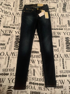 Micheal Kors Jeans 2000s - Unika Micheal Kors Selma High Waist Skinny Jeans!  Säljer dessa sällsynta och otroligt fina selma high waist skinny jeans från Micheal Kors, NY OANVÄND MED ETIKETTEN KVAR PÅ PLAGGEN (se bild) :)  Perfekta jeans för dig som är ute efter en lyxig designer denim med en vintage 2000-talskänsla!!   Storlek: 24 (motsvarar US storlek 00/XXS)  Färg: mörkblå/indigo denim med snygga guld detaljer 