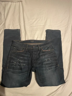 Jack & Jones Slim Straight Tim Jeans - Mörkblå jeans från Jack & Jones i modellen Slim Straight Tim. Snygga slitningar framtill, klassisk femficksdesign och kontrastsömmar. Jeansen har en rak men smal passform och är tillverkade i jeansmaterial med en cool tvättad look. Bra passform🌟🌟