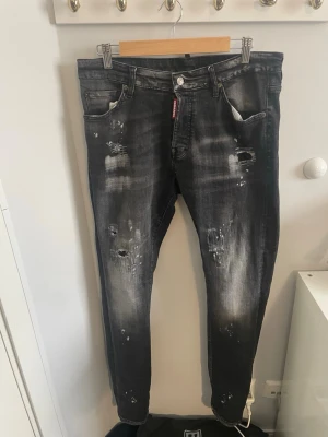   Dsquared2 jeans - Säljer ett par svarta jeans från Dsquared2 med slitningar och distressed detaljer. Jeansen har en tvättad look med ljusare partier och klassisk femficksmodell. Materialet är denim och passformen är rak med smalare ben.