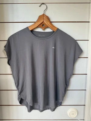 Grå tränings-topp från Röhnisch - Super härlig och fin , men tyvärr bara kommit till andvönding ett par gånger. Snygg grå t-shirt från Röhnisch med lös passform och rund hals. T-shirten har korta, vida ärmar och ett diskret logotryck fram samt stort Röhnisch-tryck på ryggen. Perfekt för träning eller chill dagar. Tillverkad i mjukt och lätt material.