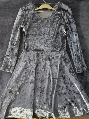 Marinblå sammetsklänning - Marinblå sammetsklänning med lång ärm och rund halsringning. Klänningen har en lätt utställd kjol och mjukt, glansigt material som ger en lyxig känsla. Perfekt för dig som gillar trendiga och bekväma plagg. Storlek 170 (S) i barnstorlek. 