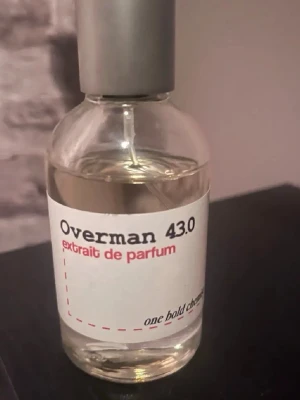 Overman 43.0 Extrait de Parfum TF ombre leather - En stilren parfymflaska från One Bold Chemist med doften Overman 43.0. Flaskan är genomskinlig med en enkel vit etikett och svart samt röd text. Locket är silverfärgat och flaskan har en modern, rund form. Perfekt för dig som gillar minimalistisk design. Avgör mängd själv. Inspirerad av tf ombre leather. 
