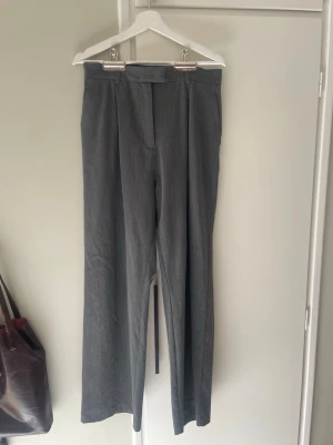 Grå kostymbyxor med raka ben - Eleganta och sköna kostymbyxor från Djerf Avenue köpta här på Plick för 900 kr. Är i mycket gott skick, har en liten fläck på framsidan men inget som är direkt märkbart.