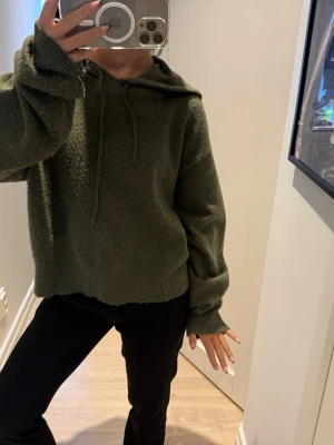 Olivgrön stickad hoodie - Mysig olivgrön stickad hoodie med huva och dragsko. Tröjan har en avslappnad passform, långa ärmar och ribbade muddar vid ärmslut och nederkant. Köpt från Zalando förra året