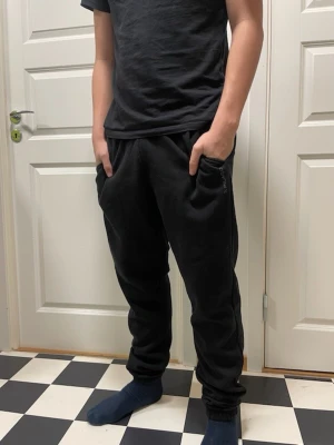 Ett par svarta byxor från Pilago  - Svarta mjukisbyxor från Pilago med elastisk midja och fickor på sidorna. Byxorna har en enkel och clean design med diskret logga på ena benet. Perfekta för chill dagar eller när du vill vara bekväm men ändå se snygg ut.