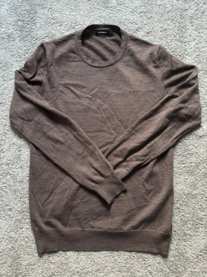 J.Lindeberg Merino tröja - Snygg brun tröja från J.Lindeberg med rund halsringning och diskret logga broderad på bröstet.  100% Merinoull. Skick 9/10. Strl M. Hör av er vid frågor eller om ni vill ha fler bilder! Skickar snabbt 🚚💨