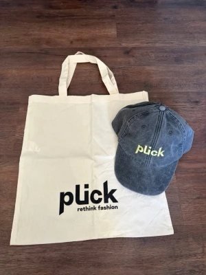 Grå keps från Plick med brodyr - Episka plick kepsen med broderad logga i gult framtill plus en tote bag med plick loggan på 