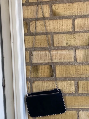 Svart axelväska med kedja från Zara - Snygg svart axelväska från Zara med silverfärgad kedjerem och detaljer längs kanterna. Materialet är mjukt tyg med metallkedja som ger en snygg vibe. Du kan ta bort kedjan och ha den som handväska också. Original priset är 249