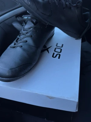 Svarta fotbollsskor från SOC - Säljer ett par svarta fotbollsskor från SOC med snörning och låg profil. Skorna har en slimmad design i syntetmaterial och platt sula, perfekta för dig som vill ha bra grepp och kontroll på planen.
