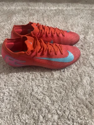 Nike Mercurial vapor 16  - Säljer ett par Nike Mercurial vapor 16 fotbollsskor i en riktigt snygg röd färg med ljusblå swoosh på sidan. Skorna har låg profil, snörning och är tillverkade i ett lätt syntetmaterial som ger bra känsla på planen. Perfekta för dig som vill sticka ut på matchen! Använda ca 4 matcher innan jag valde att lägga av med fotbollen.