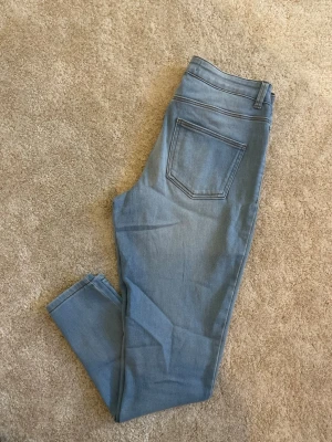 Ljusblå skinny jeans - Säljer ett par ljusblå skinny jeans med klassisk femficksdesign och hög midja. Jeansen har smal passform och är tillverkade i stretchigt denimtyg för extra komfort. Perfekta till en avslappnad vardagslook.