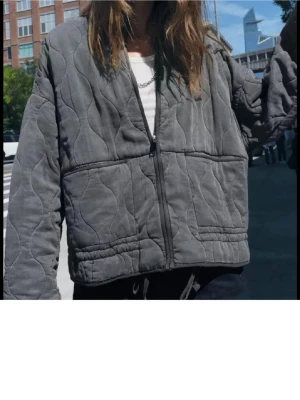 Grå quiltad jacka från zara - Snygg grå jacka med quiltat mönster och dragkedja framtill. Jackan har två stora fickor fram, hög krage och avslappnad passform. Perfekt för lager på lager och streetstyle. Materialet är mjukt och ger en mysig känsla.