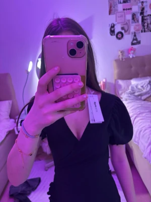 Svart omlottklänning från Gina tricot  - Snygg svart omlottklänning från gina med korta puffärmar och v-ringning. Klänningen har en feminin passform och volangdetalj nertill. Perfekt för dig som gillar en stilren look med lite extra detalj.