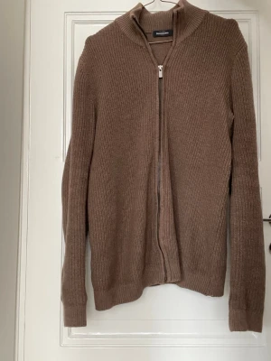 Dressmann Fullzip - Stickad beige kofta från Dressmann med hel dragkedja framtill och ribbad struktur. Koftan har lång ärm och hög krage, perfekt för lager-på-lager. Enkel och stilren design som passar till mycket.